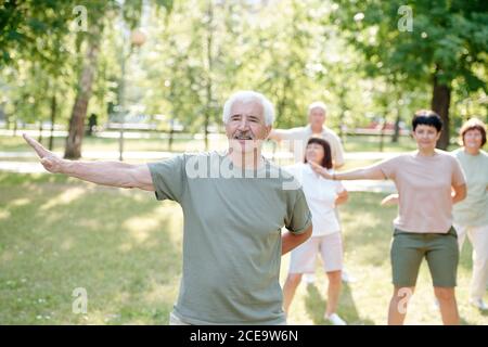 Handsome senior man with mustache practicing qigong exercise to be healthy and calm at group class in park Stock Photo