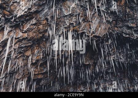 From below spiky dangerous icicles hanging on the rough rock. Stock Photo