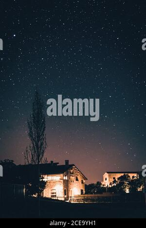 Stone houses illuminated with lamps in rural village under amazing sky with stars at night. Stock Photo