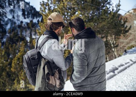 Back view of young photographers with professional camera and mobile phone standing between mountains in snow in Cerdanya, France Stock Photo