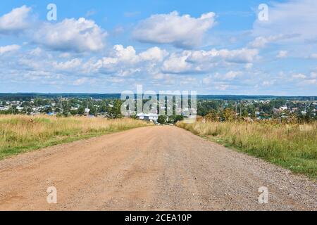 dirt road among fields on a summer day leading to the village in the background Stock Photo