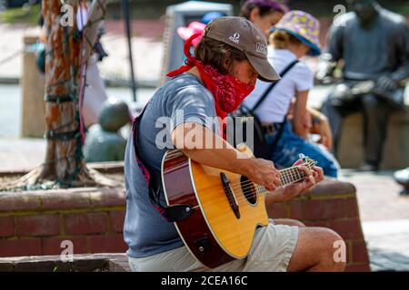 Annapolis, MD 08/21/2020: A young caucasian man is sitting on a brick wall in Annapolis marina and playing classical guitar. This street musician is w Stock Photo