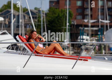 Annapolis, MD 08/21/2020: A blonde and a brunette woman are sunbathing on the deck of a yacht entering Annapolis marina. These young and beautiful wom Stock Photo