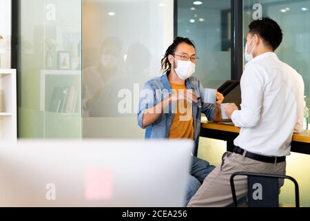 Two office workers talking while coffee break in new normal with social distance practice office.  They wear face mask reduce risk to infection of COV Stock Photo