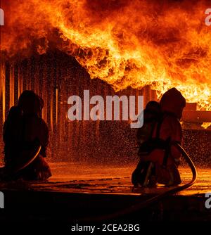Firefighters using water fog fire extinguisher to fighting with the fire flame in large building. Firefighter and industrial safety disaster and publi Stock Photo