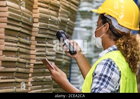 African black warehouse worker with face mask checking goods use digital tablet and barcode scanner, she wear face mask prevent from COVID-19 after fa Stock Photo