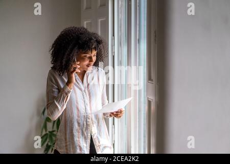 Pretty african-american businessWoman talking on smartphone holding document in hands and looking on it Stock Photo