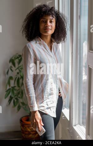 Young Woman standing at window and browsing smartphone Stock Photo