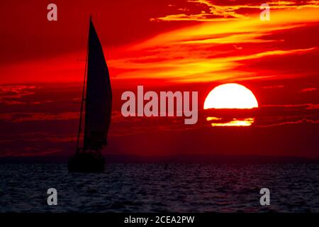 A spectacular sunset over Chesapeake Bay Maryland as captured from the east shore. Image features the large sun going down among clouds on a red sky a Stock Photo
