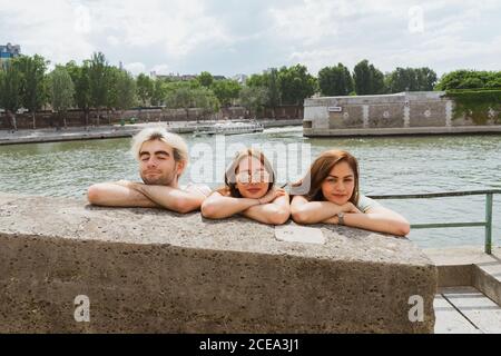 Young pretty women and handsome man with trendy haircut relaxing leaning crossing hands on stone wall on waterfront Stock Photo