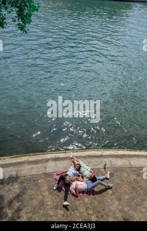 From above of happy pretty women and trendy man in casual clothes relaxing lying on each other and talking outdoors Stock Photo