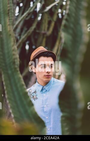 Pensive young handsome man in hat standing in cactus and looking away. Stock Photo