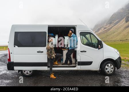 Two young men standing near nice white van while traveling through magnificent Icelandic countryside Stock Photo