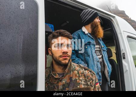 Two young men standing near nice white van while traveling through magnificent Icelandic countryside Stock Photo