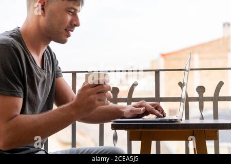 Handsome man with cup of coffee and using laptop on balcony Stock Photo