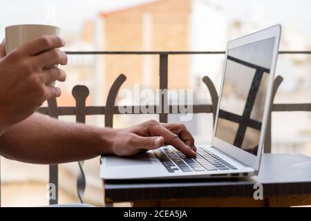 Handsome man with cup of coffee and using laptop on balcony Stock Photo