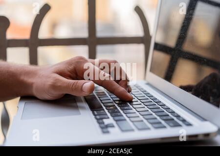 Crop male hand typing and pushing button on laptop sitting outdoors on terrace Stock Photo