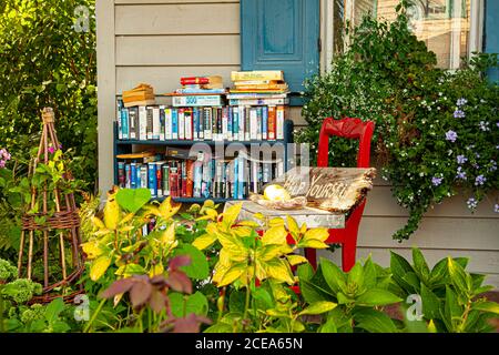 Chesapeake City, MD, USA 08/25/2020: A bookshelf full of books of different genre is placed on the porch of an old house. A  sign that reads 'Help you Stock Photo