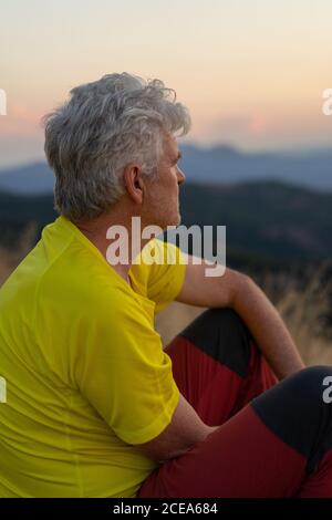 Side view of aged man looking away while sitting on Montcau mountain and resting on sunset Stock Photo