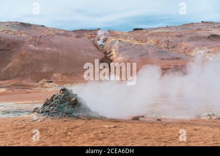 Magnificent view of hot steaming pools with mud and sulfur and piles of stones on red mountainous landscape in active geothermal zone of Namaskardh in Iceland Stock Photo