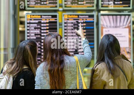 Back view long haired ladies showing by finger on flight information display in airport in Porto, Portugal Stock Photo