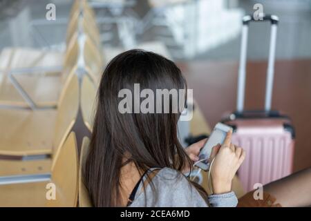 Young smiling Woman with earphones using smartphone and sitting near window Stock Photo