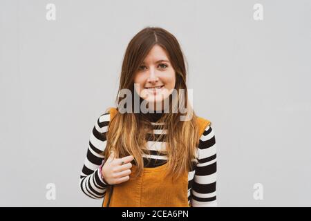 Attractive cheerful long haired lady in sweater looking at camera on grey background in Porto, Portugal Stock Photo