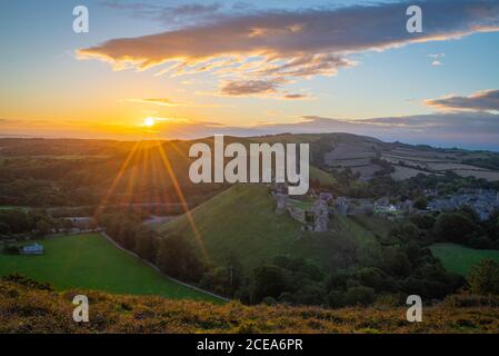 Sunrise with sunburst over the Dorset Countryside with Corfe castle and hills glowing from the morning sun. Stock Photo