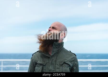 Thoughtful bearded man standing on ship deck and looking away at the ocean. Stock Photo