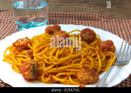 Plate of spaghetti with meatballs and tomato sauce on a traditional table next to a glass of water Stock Photo