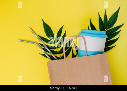 Paper bag with bamboo cup and reusable drinking straws on yellow background. Mockup, top view. Plastic free concept Stock Photo
