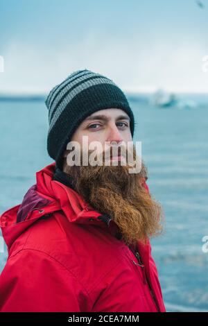 Crop handsome bearded male in warm clothes looking at camera on water background in Skaftafell, Iceland and Vatnajokull Stock Photo