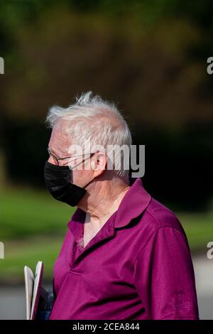 Rock Hall, MD, USA 08/18/2020: The new normal due to COVID-19 pandemic. An elderly man in his eighties is carrying a newspaper in the street. He is we Stock Photo