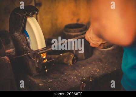 Crop smith using grindstone to sharpen metal blade in professional workshop Stock Photo