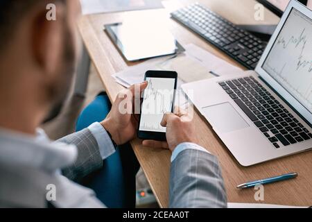 Stock Traiding. Trader sitting at office holding using online app on smartphone for monitoring chart cryptocurrency flow close-up Stock Photo