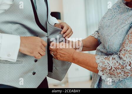 Side view of crop Woman helping to button up waistcoat of male in white shirt Stock Photo