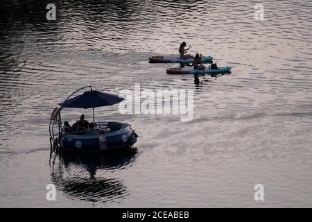 Austin, Texas, USA, Aug. 18, 2020: A couple on stand-up paddle boards and people in a round inflatable raft enjoy sunset after a hot summer day on Lady Bird Lake in downtown Austin. ©Bob Daemmrich Stock Photo