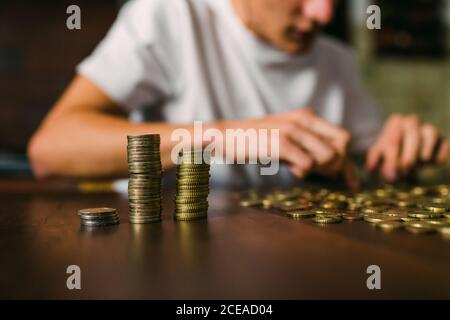 anonymous young man counting shiny coins and stacking them on wooden table Stock Photo