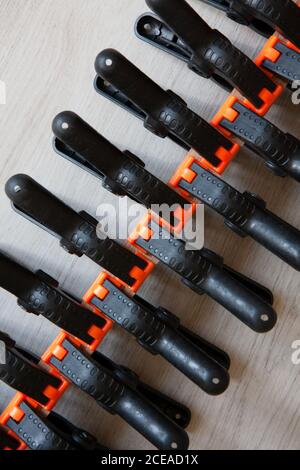 Pattern from black and orange construction clamps. A set of medium plastic clips. Clamping tools for carpentry work. Hand tools for needlework. Clampi Stock Photo