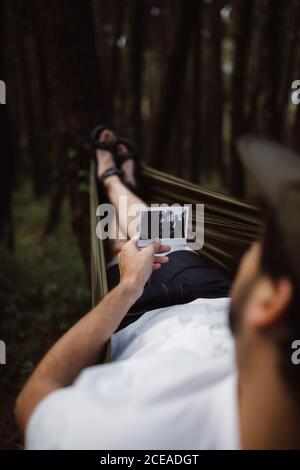 Back view of man lying in hammock in forest and looking at photo in Cantabria, Spain Stock Photo