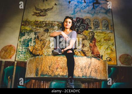 Lovely young Woman looking at camera while sitting on stone table in abandoned building. Stock Photo