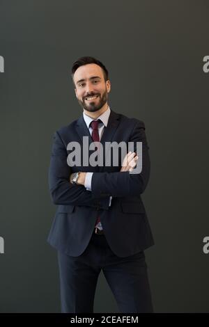 Smiling unshaven male in black business attire with wristwatch looking at camera standing with folded arms over black background Stock Photo