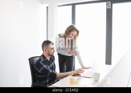 Smiling Woman and man at office desk watching laptop together and working in team inside of modern office Stock Photo
