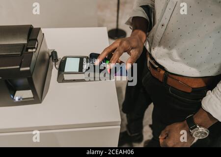 From above shot of hand of African American man pushing buttons on keypad of modern payment terminal Stock Photo