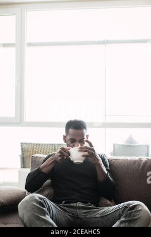Pensive black man on sofa drinking coffee Stock Photo
