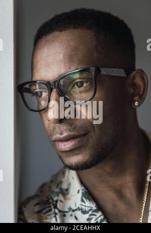 Head shot of serious adult African American man in golden accessories and glasses touching chin Stock Photo