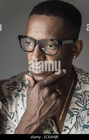 Head shot of serious adult African American man in golden accessories and glasses touching chin Stock Photo