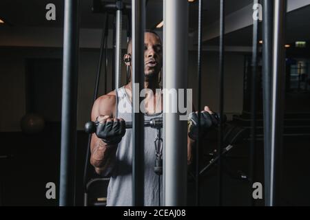 Handsome African American guy in earphones exercising on machine while working out in modern gym Stock Photo