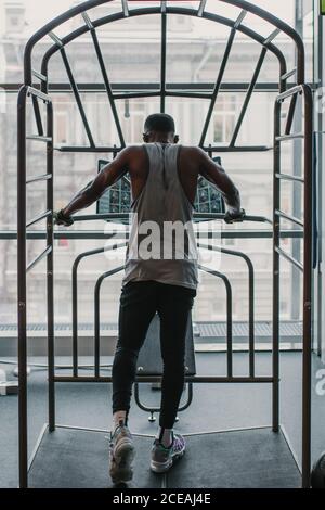 Back view of African American guy in sportswear using gym equipment while working out near window Stock Photo