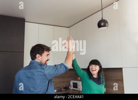 Cheerful young man and Woman giving high five to each other while standing in modern kitchen together Stock Photo